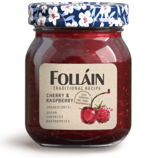 Glass jar of Folláin Cherry and Raspberry jam with an illustrated floral lid and ingredients label, including sugar, cherries and raspberries