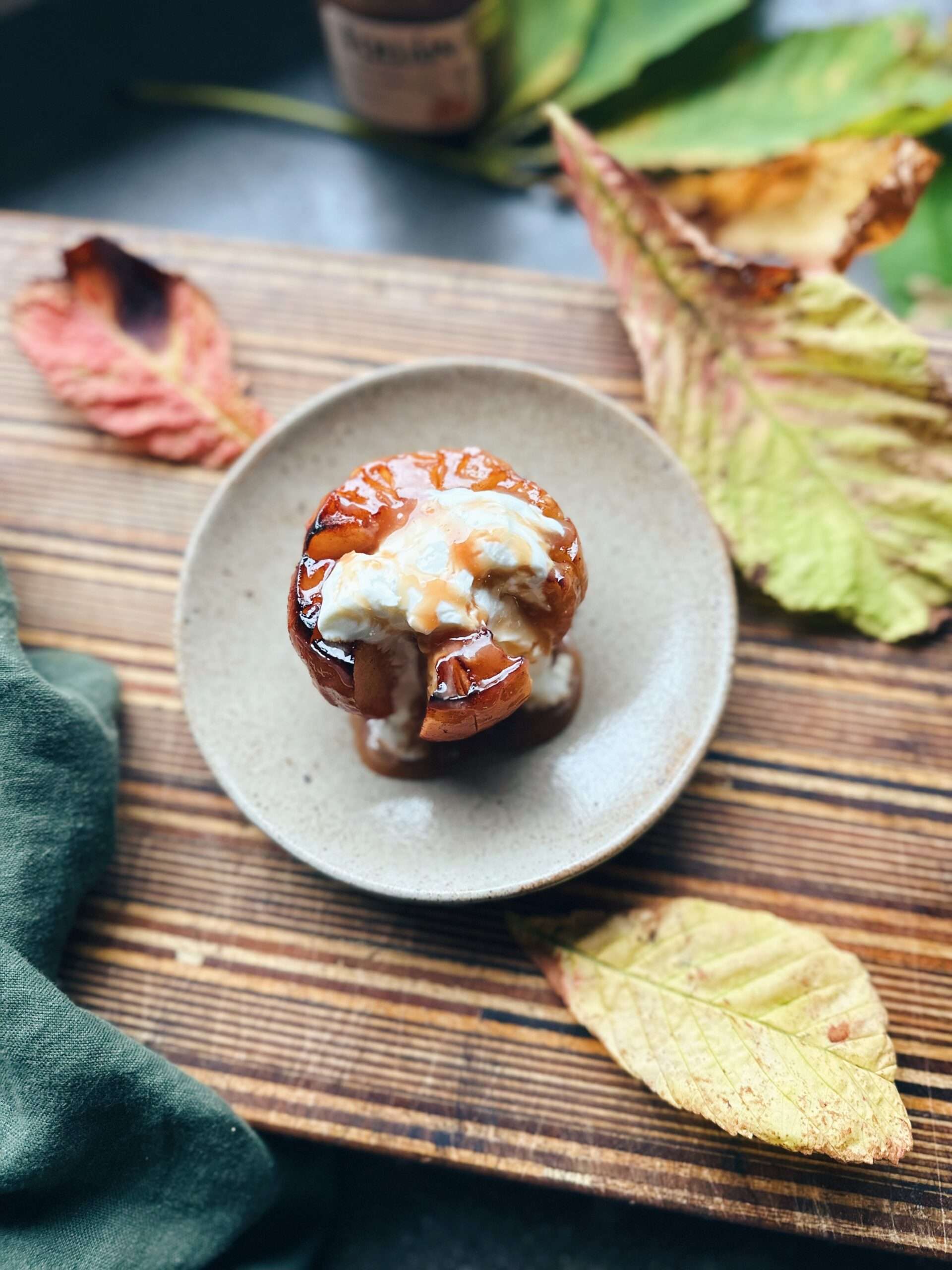 Baked cut apple on plate on chopping board with irish cream liqueur and greek yogurt decorative autumn leaves surrounding plate